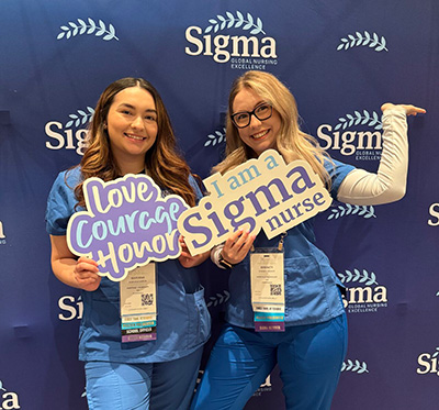 Two members at NSNA holding props that say: Love Courage Honor and I am a Sigma nurse.